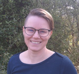 Deborah smiles at the camera. She has brown hair swept to one side and she wears round glasses.
